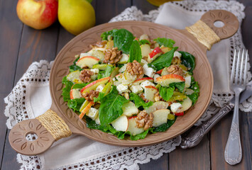 Apple Pear Spinach Salad with crumbled feta cheese, toasted nuts and honey lemon vinaigrette dressing served on a wooden plate.
