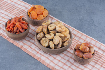 Tasty dried fruits in bowls on the towel, on the marble background