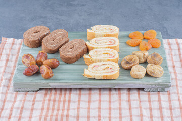 Roll cake and dried fruits on the board , on the marble background