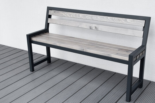 Metal wooden benche on grey terrace on light house wall background outdoors.
