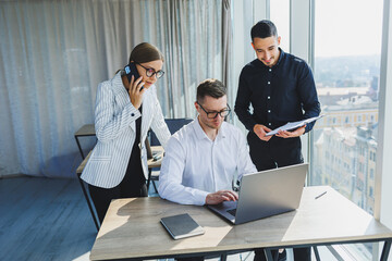 Group of business people in casual clothes talking to each other in office and using gadgets while working on business startup in modern workspace