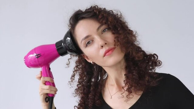 Woman gives herself a curly hairstyle. Hair care concept. A curly woman dries her hair at home with a hair dryer with a diffuser attachment. A beautiful girl uses a modern hair dryer.