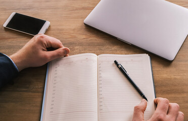 Close up top view of businessman writing in notebook, caucasian male hands holding pen making notes planning new appointments information in organizer personal paper planner at desk