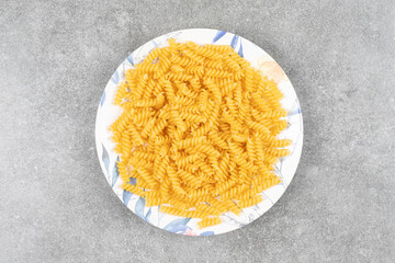 Plate of raw fusilli on marble surface
