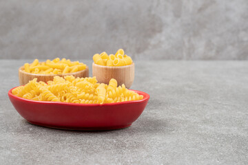 Bowls of various uncooked pasta on marble background