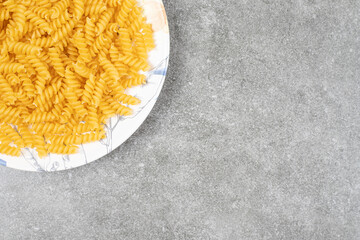 Plate of raw fusilli on marble surface