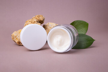 Open cosmetics container with white cream and glossy green leafs on background,eco friendly concept.