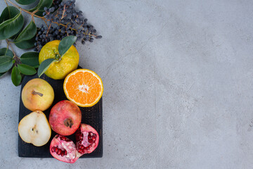 Decorative leaves with sliced and whole pears, pomegranates and tangerines on a black board on marble background