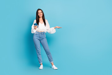 Fototapeta na wymiar Full length portrait of attractive cheerful person hold telephone arm demonstrate empty space isolated on blue color background