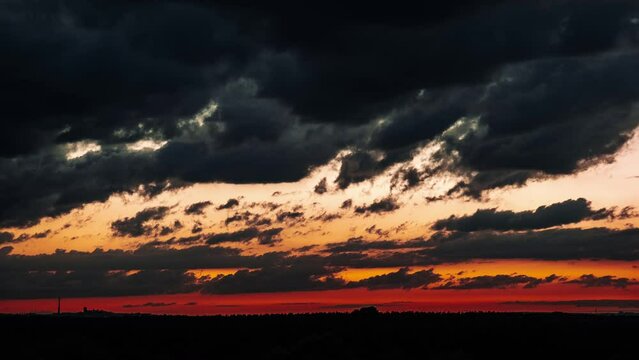 Timelapse of clouds after sunset moving in orange colorful sky. Vibrant gold-colored twilight cloudscape. Scenic time lapse vibrant red and orange sky as dark clouds light up with color during sunset