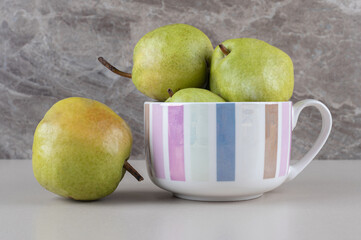 Delicious pears in and next to a large mug on marble background