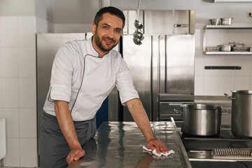 Young handsome male chef cleaning his workplace on kitchen in restaurant