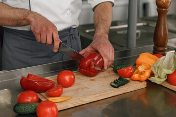 Busy chef cutting red pepper and cucumbers on a board for making salad in modern restaurant kitchen