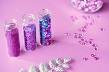 Obraz na płótnie Canvas All kinds of glitter products on pink sparkling background. Close-up on vials, bottles with various glitter makeup in neon pink, blue and turquoise shades. Scattered strasses, rhinestones.