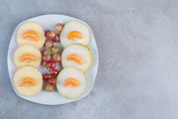 Sliced apples, pears, tangerines and grapes on a platter on marble background
