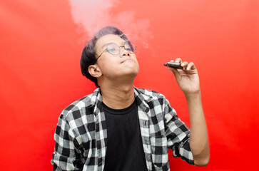 asian man holding a vape device and surounded by cloud of smoke. vaping and smoking concept.