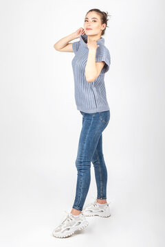 Studio portrait of gorgeous brunette woman with beautiful body shape wearing blue sweater without sleeves, jeans and sport shoes. Model looking at camera. Image contains motion blur and noise