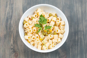 Delicious macaroni with peas and greens on a wooden table