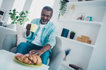 Portrait of nice satisfied peaceful person sitting chair enjoy fresh hot coffee croissant free time weekend indoors