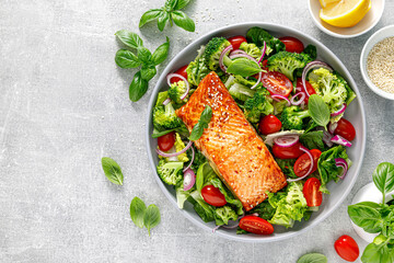 Grilled salmon fish fillet and fresh green leafy vegetable salad with tomatoes, red onion and...
