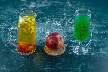 natural juice in a carafe, a glass of processed juice and apple on the blue background
