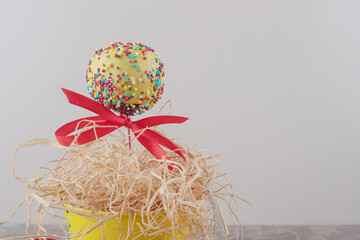 A ribbon adorned lollipop and a small pile of straw in a bucket on marble background