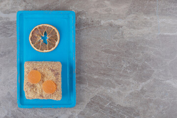 A cake with marmelades next to a dried slice of lemon on a blue platter on marble background