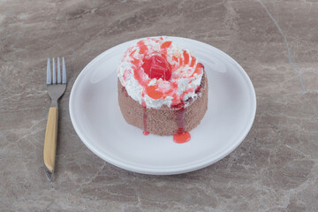 A small cake with cream and strawberry syrup topping on a plate on marble background