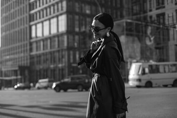 Girl on the street in a black coat. Stylish girl in a black raincoat on the background of a high glass house