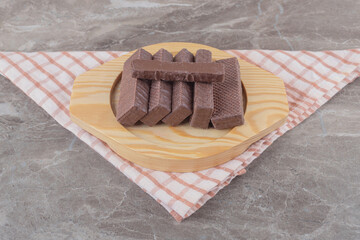 Chocolate coated wafers on a wooden platter on marble background