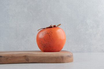 Single persimmon fruit on wooden board