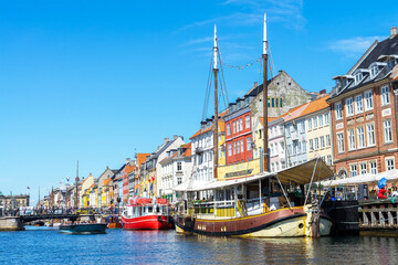 Nyhavn is waterfront and canal in Copenhagen, Denmark. Colourful facades of houses and old ships along canal. Wooden ships moored in canal