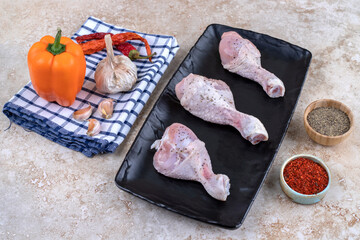 Uncooked chicken legs meat with vegetables on a dark board