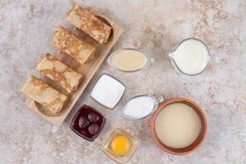 A wooden board of tasty crepes and strawberry jam