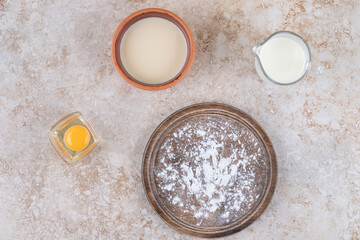 A brown plate of flour and raw eggs with a glass cup of milk