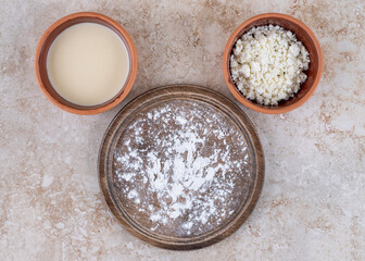 A brown plate of flour and a clay bowl of cottage cheese
