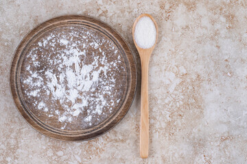 A brown plate of flour and a wooden spoon of sugar
