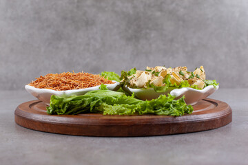A wooden board of raw macaroni with lettuce and greens