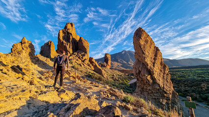 Man with backpack hiking with scenic golden hour sunrise morning view on unique rock formation Roque Cinchado, Roques de Garcia, Tenerife, Canary Island, Spain, Europe. Pico del Teide volcano summit