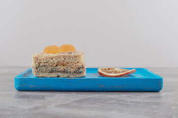 A cake with marmelades next to a dried slice of lemon on a blue platter on marble background