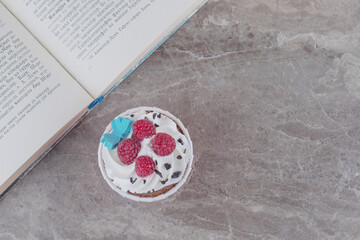 A cupcake and an open book on marble background