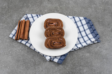 Chocolate cake roll on white plate with cinnamon