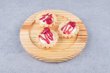 Cupcakes with strawberry syrup topping on a wooden platter on marble background