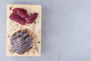 Chocolate coated cake and red pine cones on a board on marble background