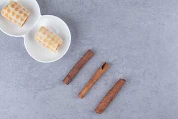 Caramel-filled waffle rolls on a platter next to cinnamon sticks on marble background