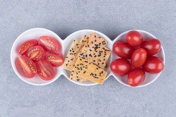 Serving platter with piles of tomatoes and sliced bread with sesame topping on marble background