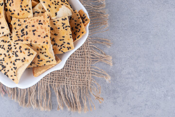 Sesame coated bread slices on a platter on a piece of cloth on marble background