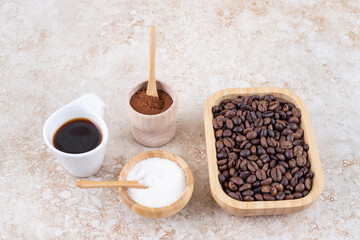 An arrangement of coffee cup, sugar, ground coffee powder and a pile of coffee beans in a wooden platter on marble background