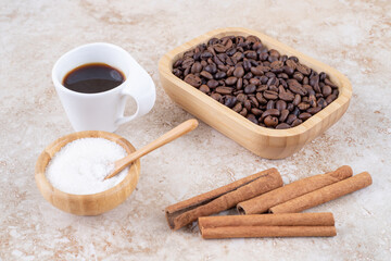 Cinnamon sticks, coffee beans, sugar and a cup of coffee on marble background