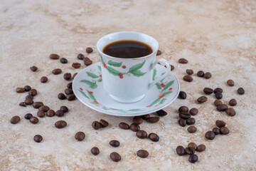Scattered coffee beans around a cup of coffee on marble background